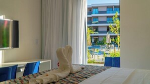 Habitación de hotel con cama, televisor de pantalla plana, mesa de comedor y vistas a una piscina y un edificio.