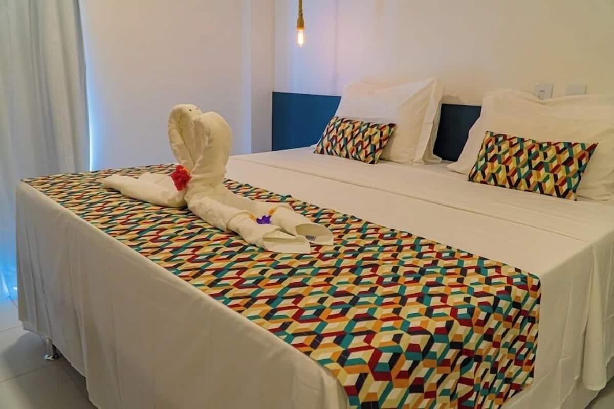 Een hotelkamer met een bed, een kleurrijk bed met een geometrisch patroon en een handdoek met een bloem.