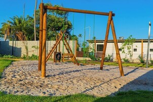 Un columpio de madera en una zona arenosa, con una valla y árboles al fondo.