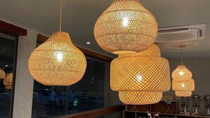 Un comedor con una mesa redonda dispuesta para cuatro personas, rodeada de sillas de madera. Hay tres lámparas colgantes grandes de fibra suspendidas del techo.