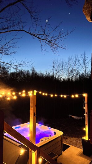 A hot tub with a wooden frame, surrounded by string lights, set against a night sky with visible stars. - Cozy Cabin Escape w/Hot Tub, King Bed & Fire Pit (New Lexington)