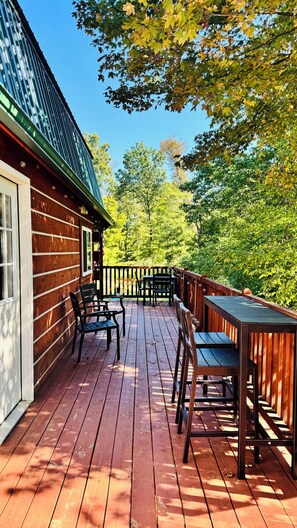 A wooden deck with outdoor furniture, a building with a green roof, and trees in the background. - Cozy Cabin Escape w/Hot Tub, King Bed & Fire Pit (New Lexington)