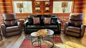 Ein gemütliches Blockhäuschen-Interieur mit einer schwarzen Ledersofa, zwei Ledersesseln, einem kleinen runden Tisch und einem Holzboden.