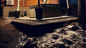 Eine Blockhütte mit Steinfundament, einer Veranda und einem kleinen Schuppen.