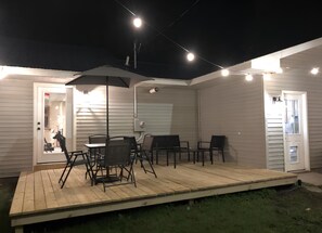 A covered outdoor patio with a table and chairs, a wooden deck, and string lights.