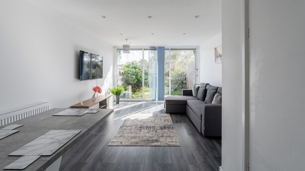 A modern living room with a grey sofa, a wooden coffee table, and a large window with a view of greenery. - Karazo Property- Luxury 2 bed in Croydon (Croydon)