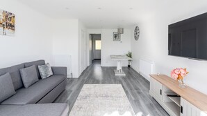 A modern living room with a grey sofa, a wooden side table, and a large flat-screen TV mounted on the wall. - Karazo Property- Luxury 2 bed in Croydon (Croydon)