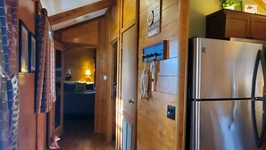 A wooden interior with a kitchen area featuring a stainless steel refrigerator, wooden cabinets, and a bed in the background. - Lakefront Magic Wilderness Cabin (Leesburg)