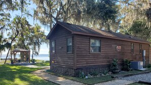 A wooden cabin with a stone foundation, a porch, and a view of the water. - Lakefront Magic Wilderness Cabin (Leesburg)