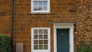 A stone house with a dark blue door, a small window, and a white-framed window above.