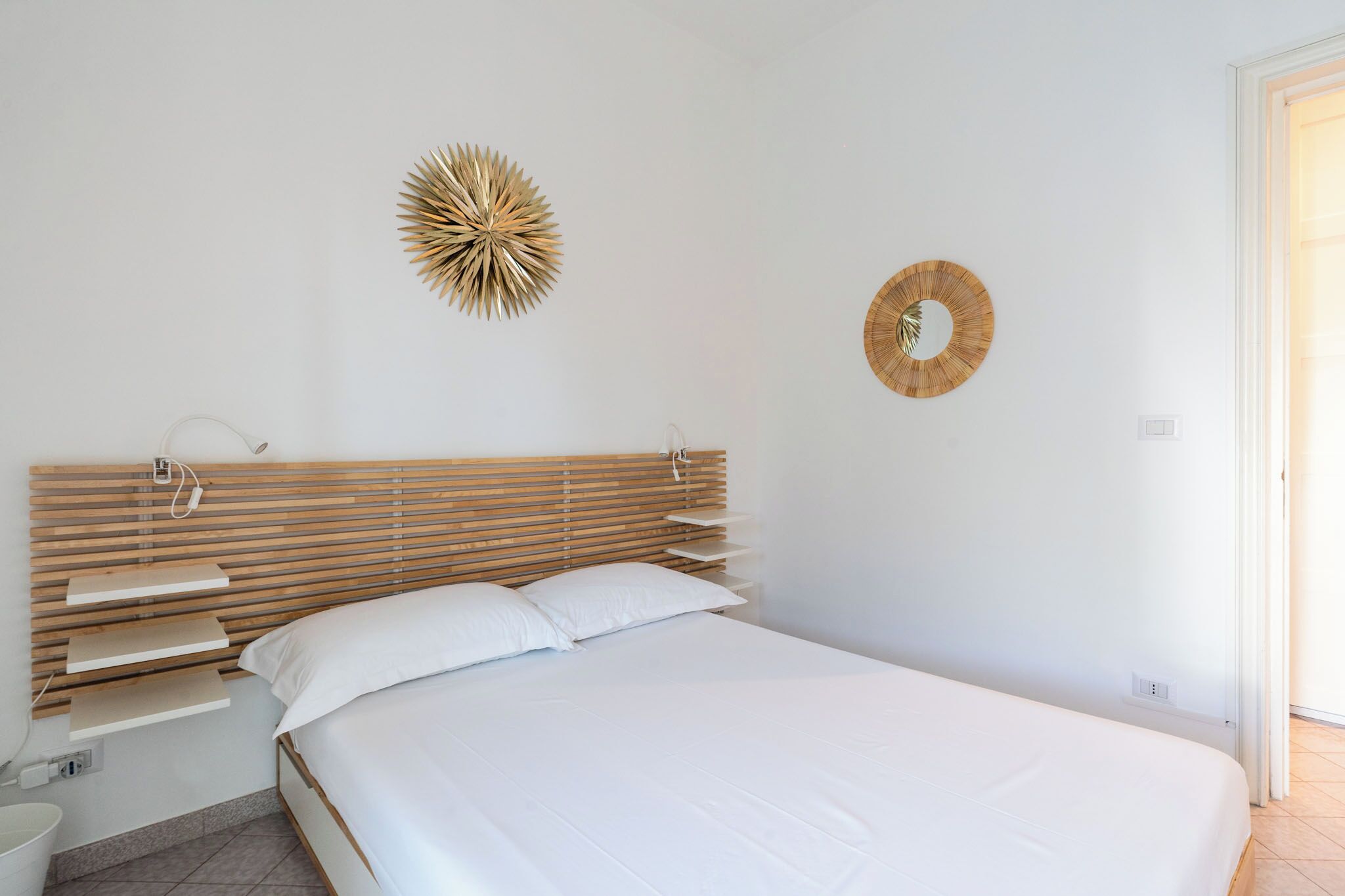 A bedroom with a wooden slatted headboard, white bedding, and two wall-mounted decorative items.
