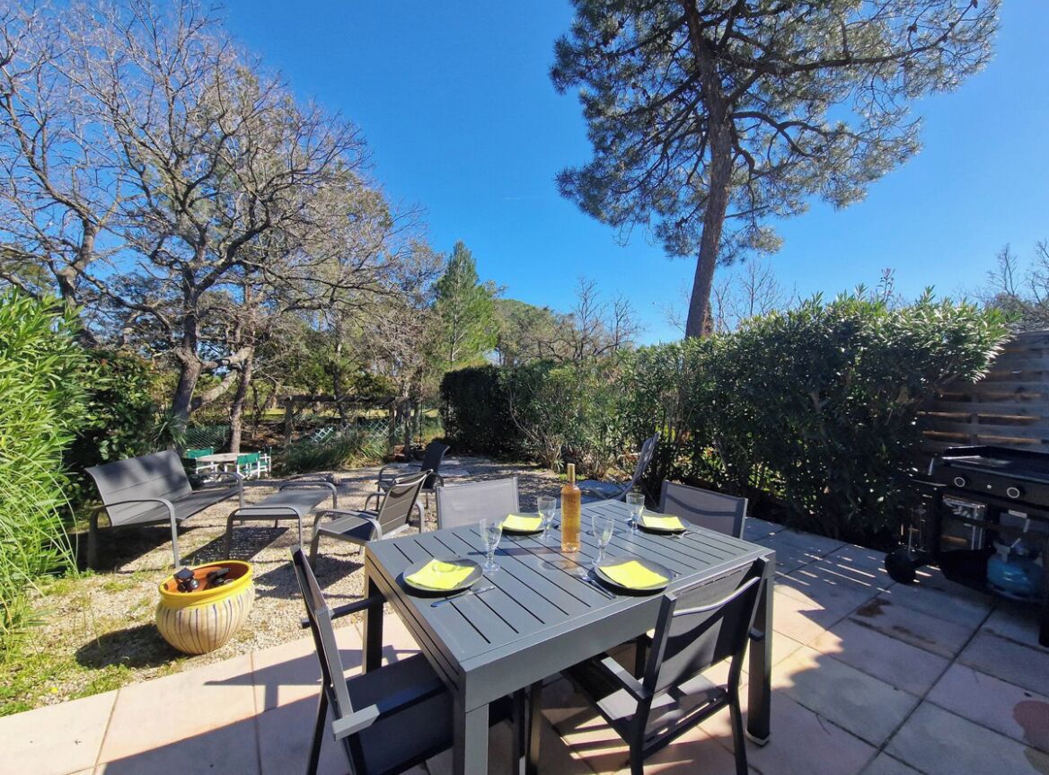 Une terrasse extérieure avec une table dressée pour quatre personnes, entourée de chaises, d’un barbecue et d’un coin salon avec un banc.