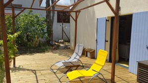 Une terrasse en bois avec deux chaises longues, une jaune et une blanche, placée sous une pergola en bois.