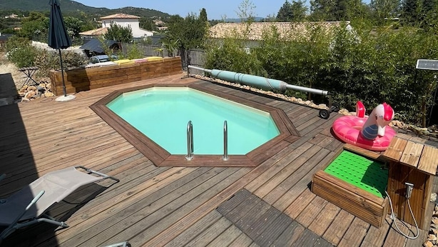 Une terrasse en bois avec une piscine rectangulaire, une chaise longue et une petite piscine gonflable avec une figurine.