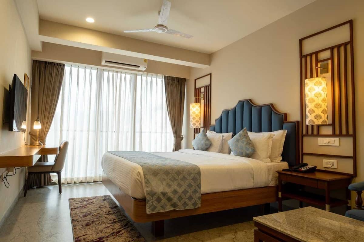 A hotel room with a bed, bedside table, desk, chair, and an air conditioning unit.