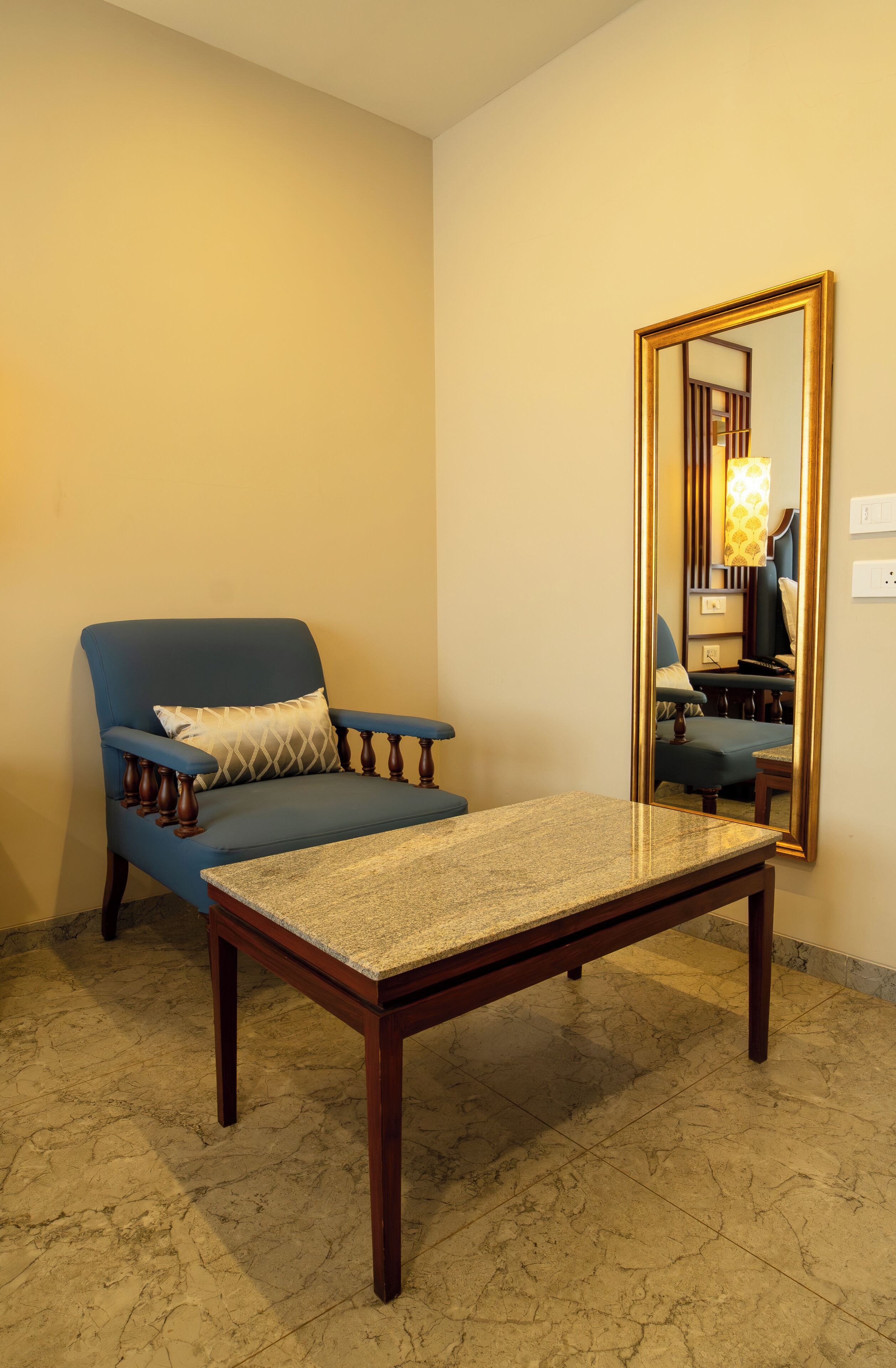 Una habitación con un sillón azul, una mesa de centro de madera y un espejo grande en la pared.