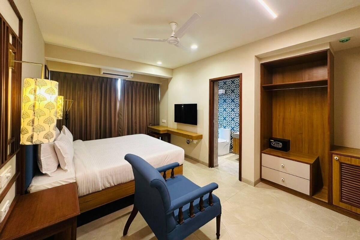 A hotel room with a bed, a desk, a chair, a wardrobe, a television, and a ceiling fan.