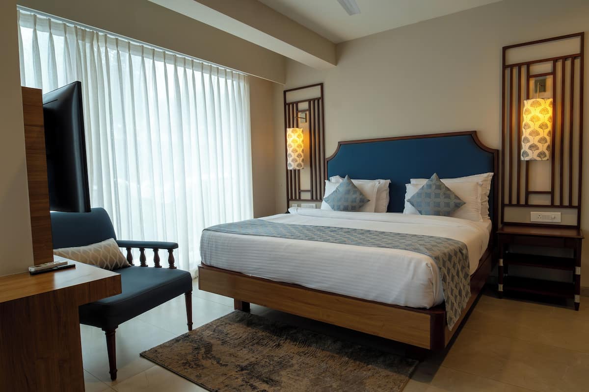 A hotel room with a large bed, a desk with a chair, a television, and a window with curtains.