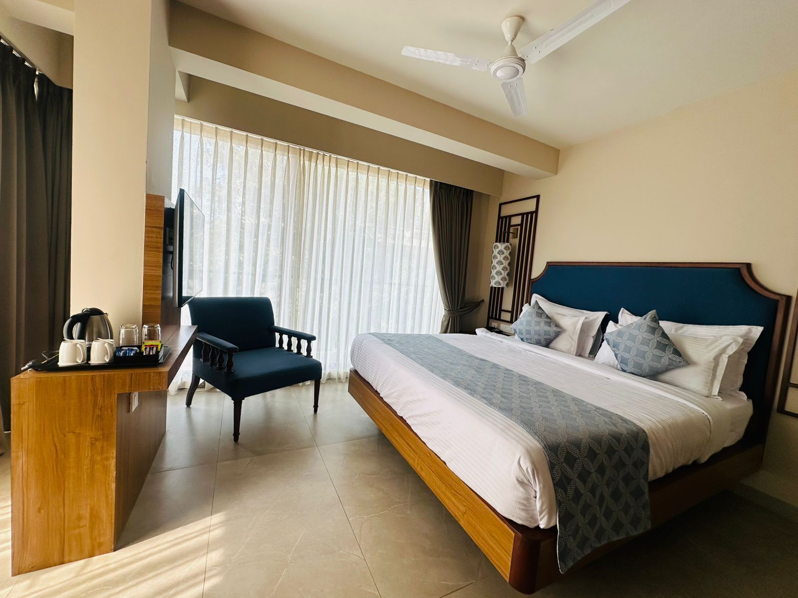 Een hotelkamer met een bed, een bureau, een stoel en een plafondventilator.