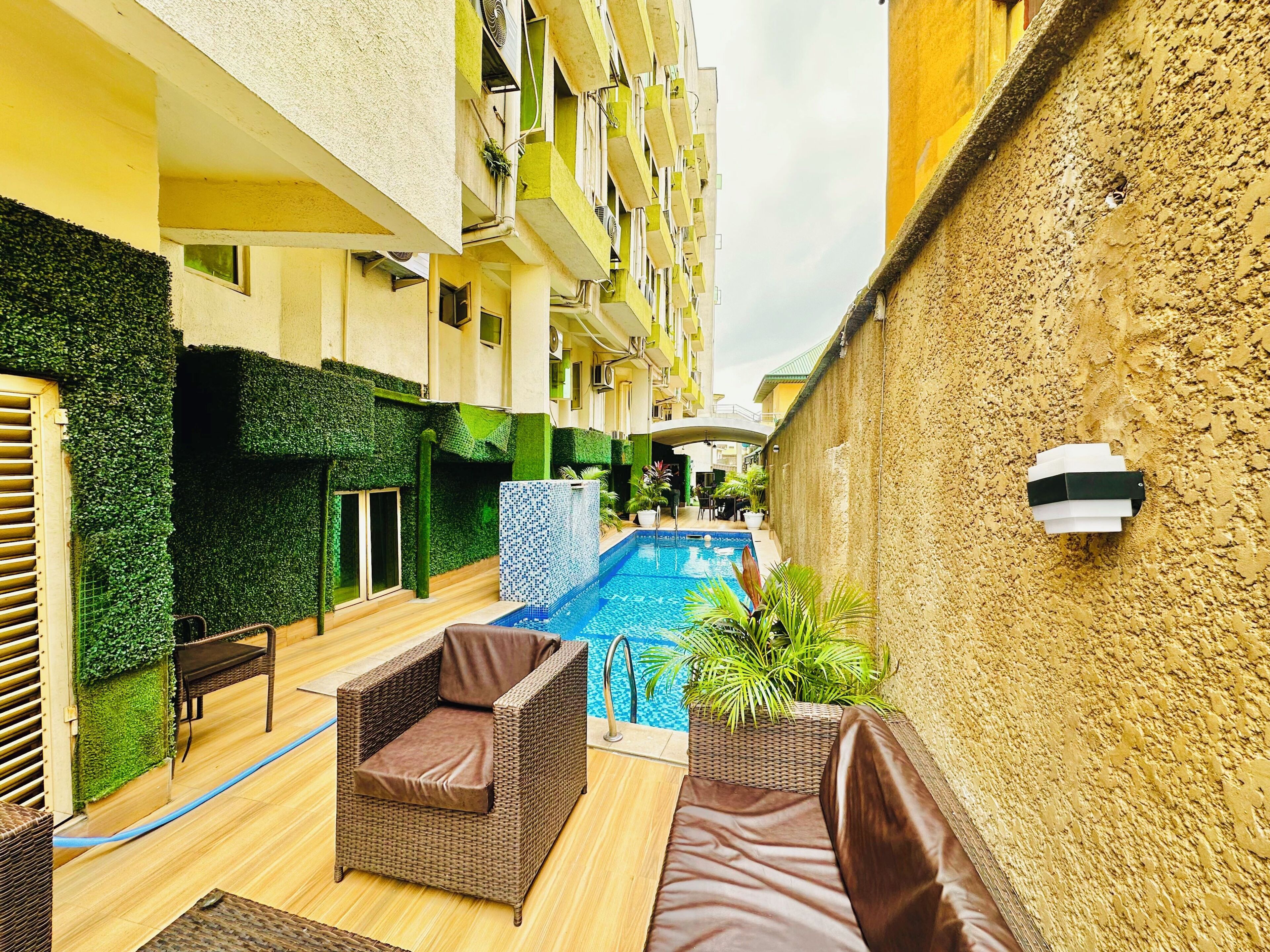 An outdoor swimming pool area with wicker furniture and a tiled wall.