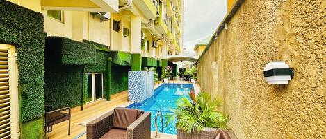 An outdoor swimming pool area with wicker furniture and a tiled wall.