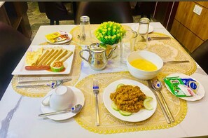 Ruokapöytä on katettu erilaisilla ruokalajeilla, kuten lautasella olevilla makkaraviipaleilla, kulhossa olevalla keitolla ja lautasella olevalla paistetulla ruoalla. Lisäksi pöydällä on mausteita ja ruokailuvälineitä.