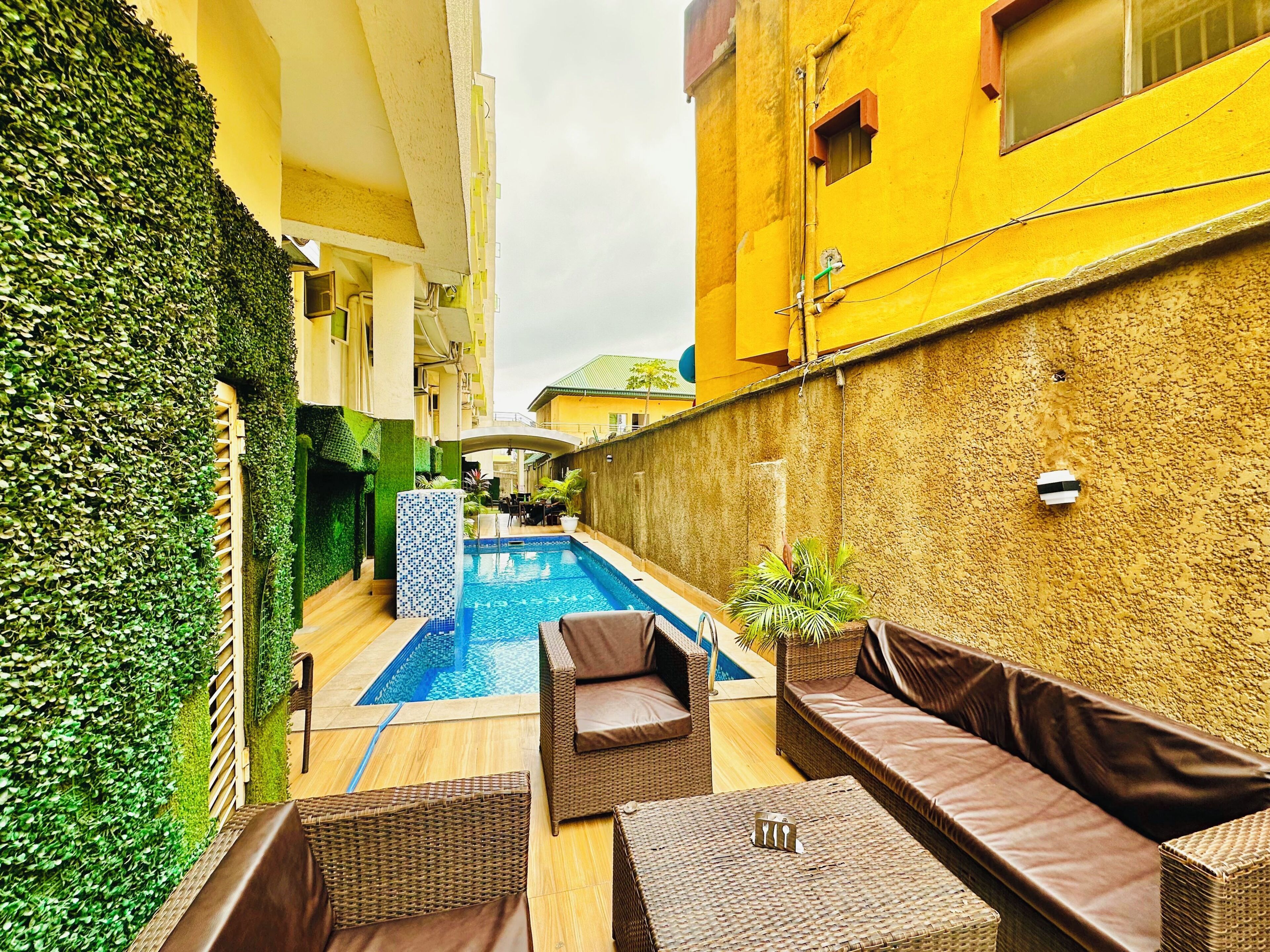 A pool area with a small pool, wicker furniture, and a green wall.