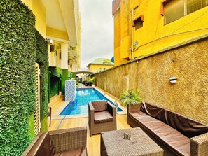 Uma área de piscina com uma piscina pequena, móveis de vime e uma parede verde.