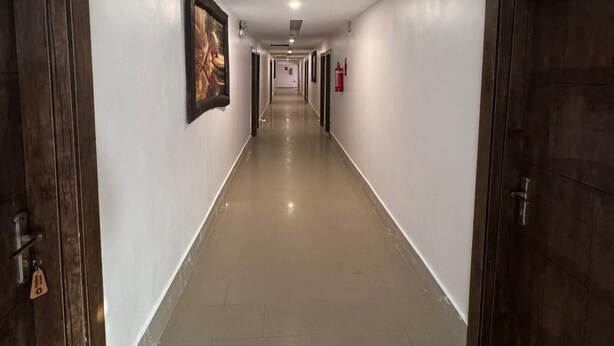 A long, narrow hallway with white walls and a shiny floor, flanked by wooden doors and a fire extinguisher on the right wall. - PRESKEN HOTEL ALADE (Lagos)
