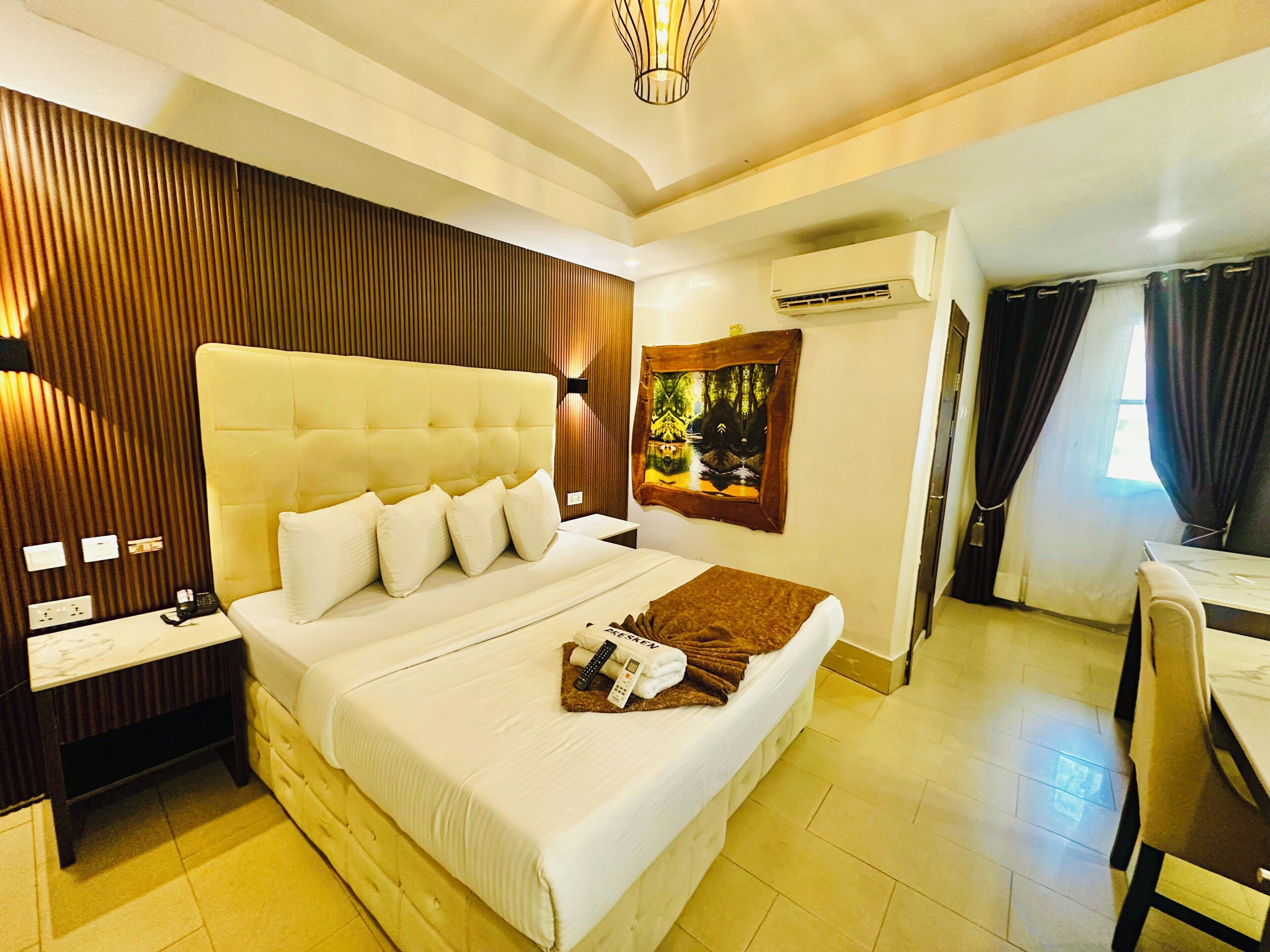 Habitación de hotel con una cama grande, una mesita de noche, un equipo de aire acondicionado y un cuadro en la pared.