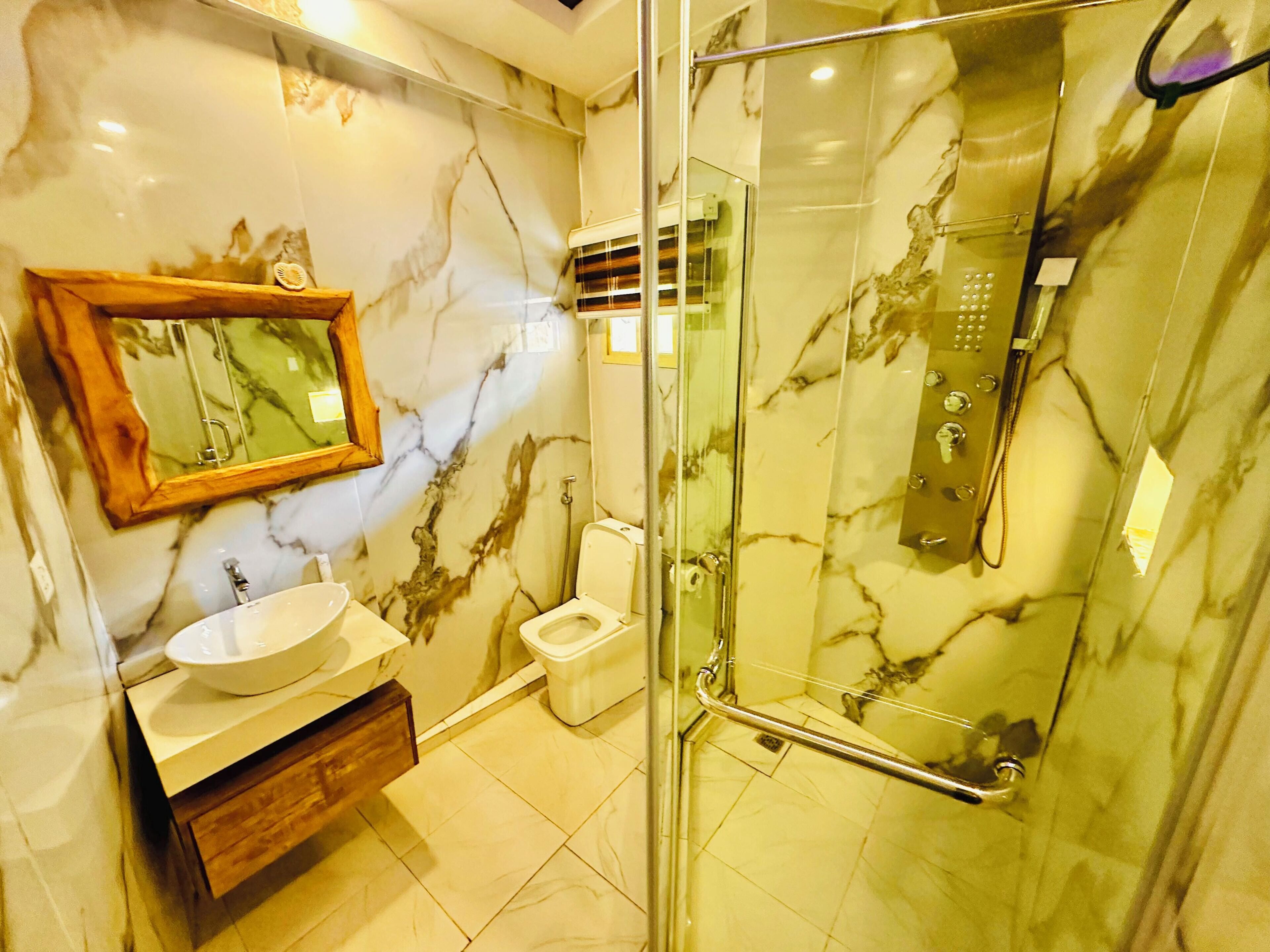A bathroom with a marble wall, a sink, a toilet, and a glass-enclosed shower area.