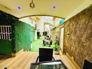 Un pati interior amb zona de menjador, paret vegetal i vista al carrer.