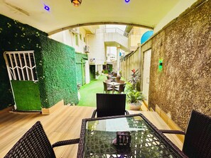 Uma área de refeições interna com mesa de vidro, cadeiras de vime e uma parede verde.