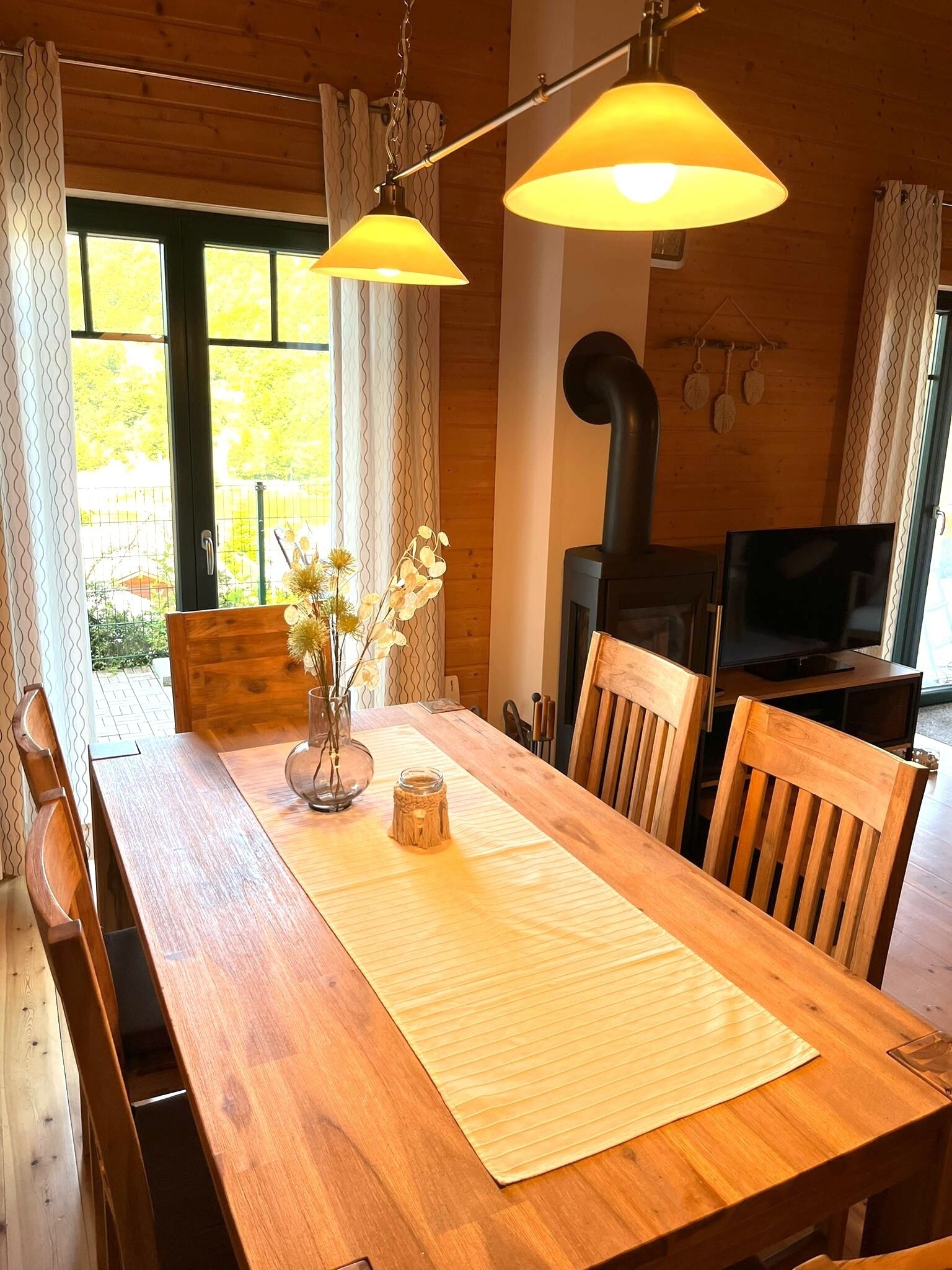 A wooden dining table with chairs, a vase with flowers, and a wooden bench.