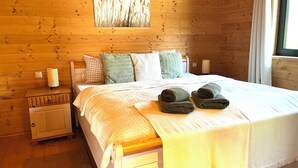 A wooden-paneled bedroom with a bed, pillows, a bedside lamp, and a window with curtains.