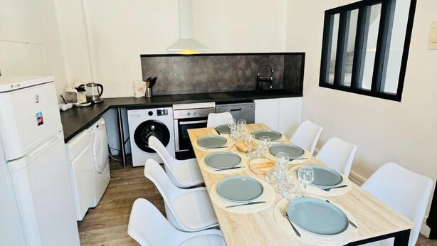 A compact kitchen with modern appliances, a dining area with a wooden table set for four, and a large window with blinds. - Town house 10 min from Futuroscope (Migné-Auxances)