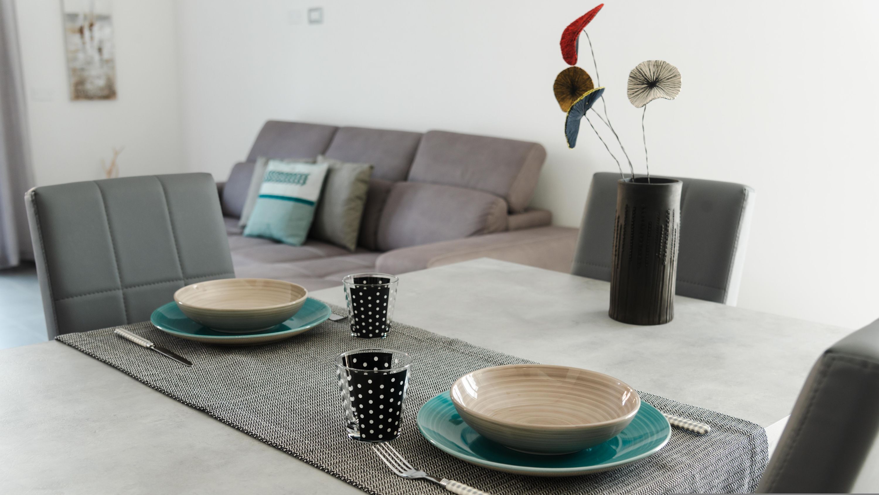 Una mesa de comedor con dos platos, un salero y un vaso. Un jarrón con flores secas está sobre la mesa.