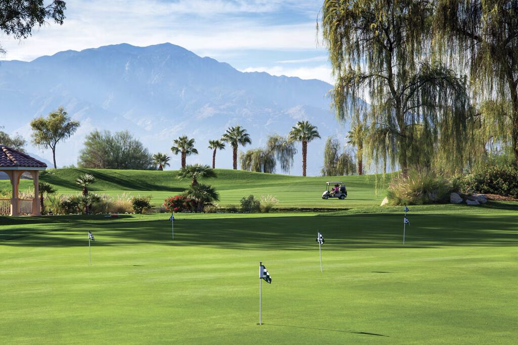 A golf course with a gazebo, palm trees, and mountains in the background.