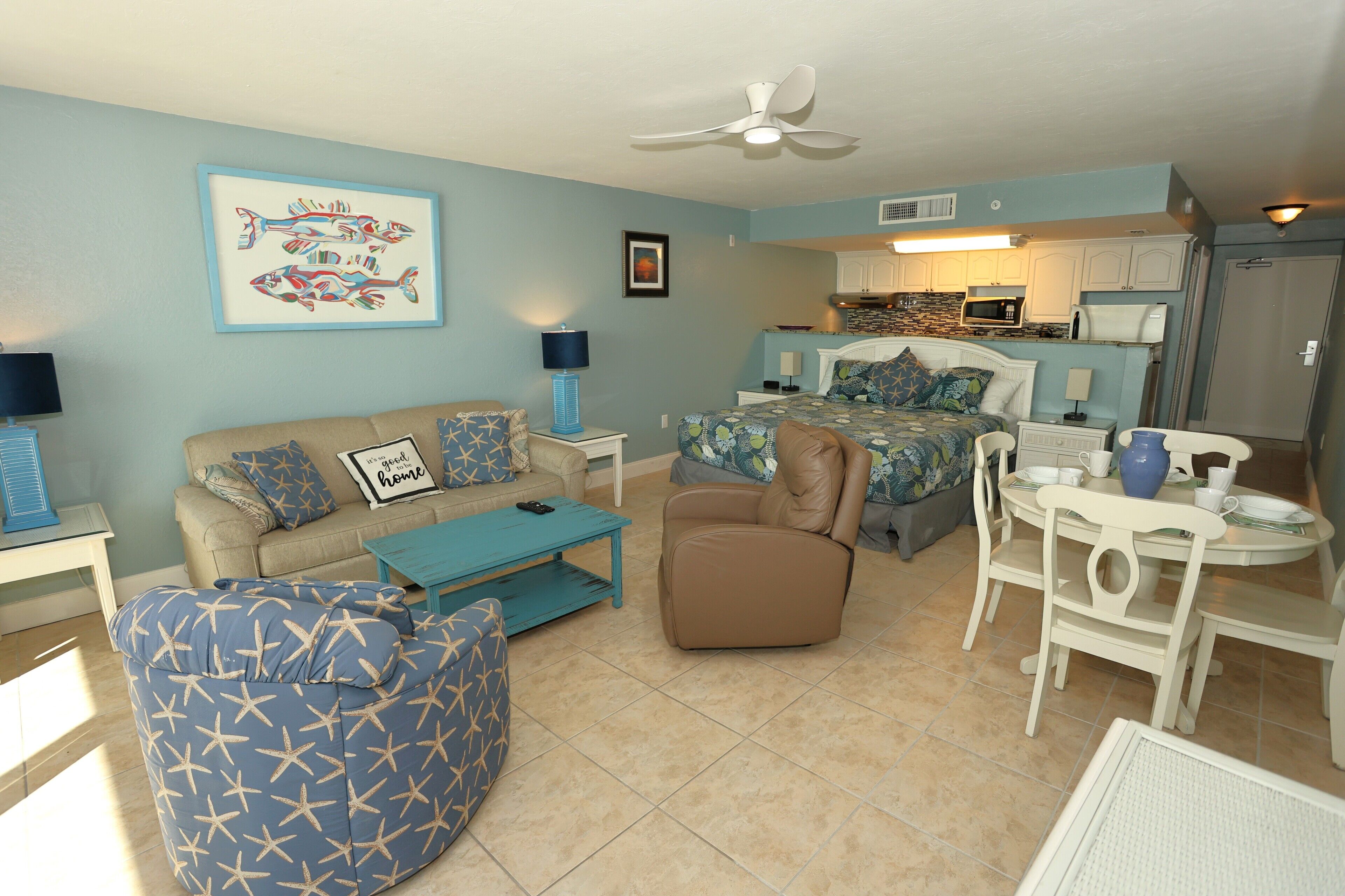 A living room with a sofa, armchair, and coffee table, a dining area with a table and chairs, and a kitchenette with a microwave and stove.