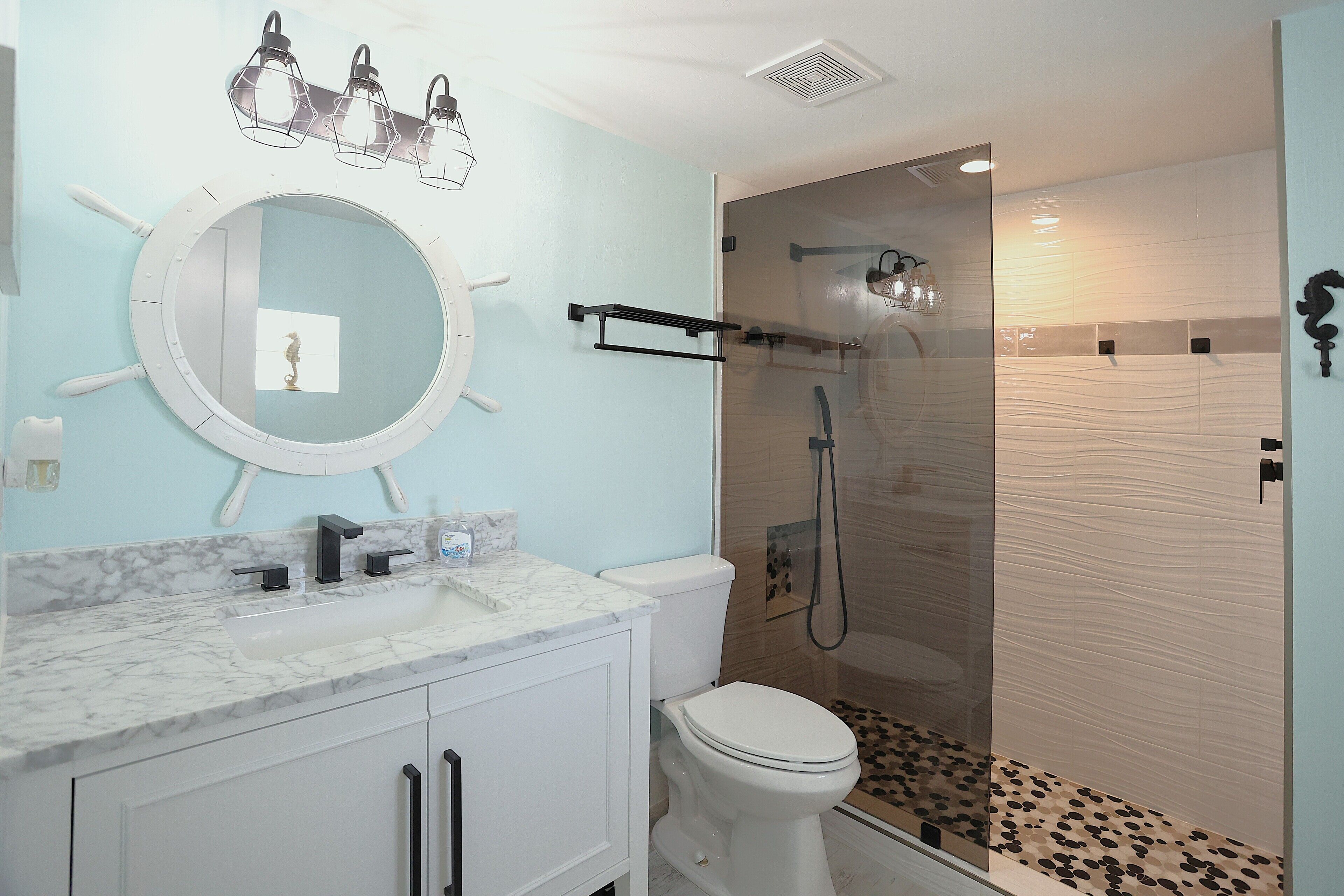 A bathroom with a white toilet, a round mirror, a marble sink, and a glass-enclosed shower.