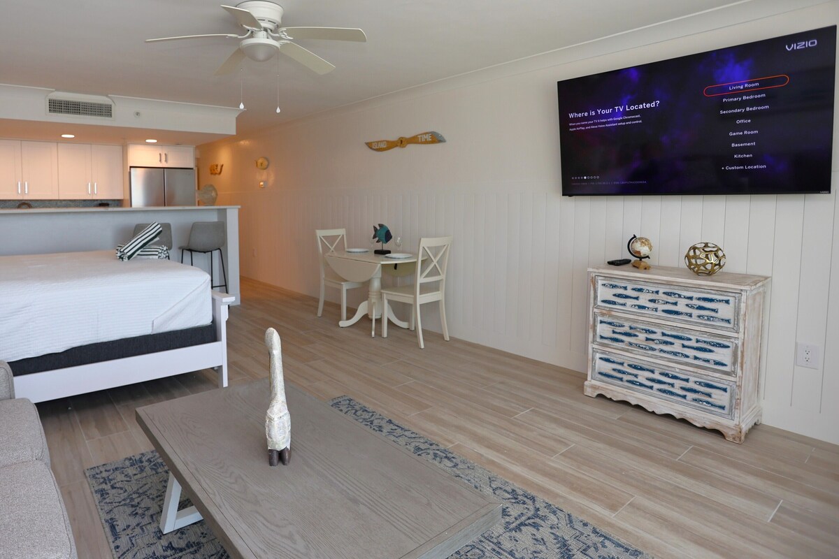 Een moderne woonkamer met een bed, een eethoek, een keuken en een televisie waarop een menu van een locatiedienst wordt getoond.