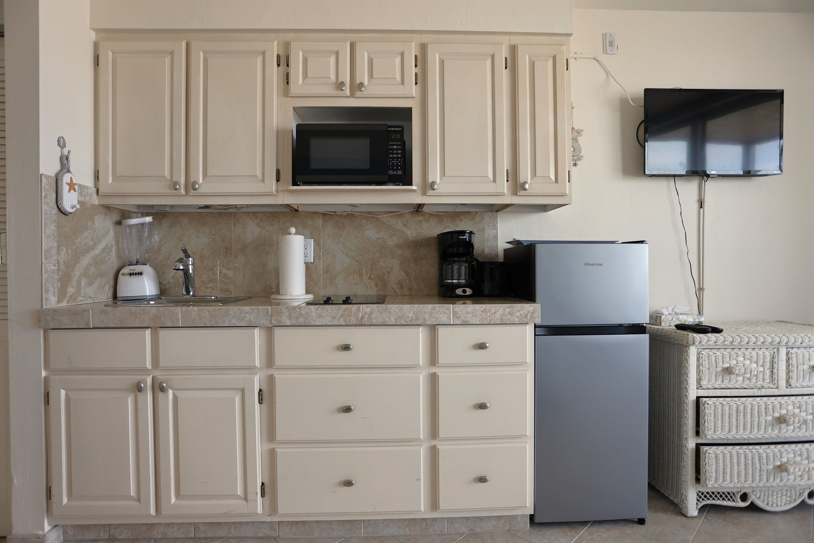 Una cocina con armarios color beige, microondas, cafetera y refrigerador.