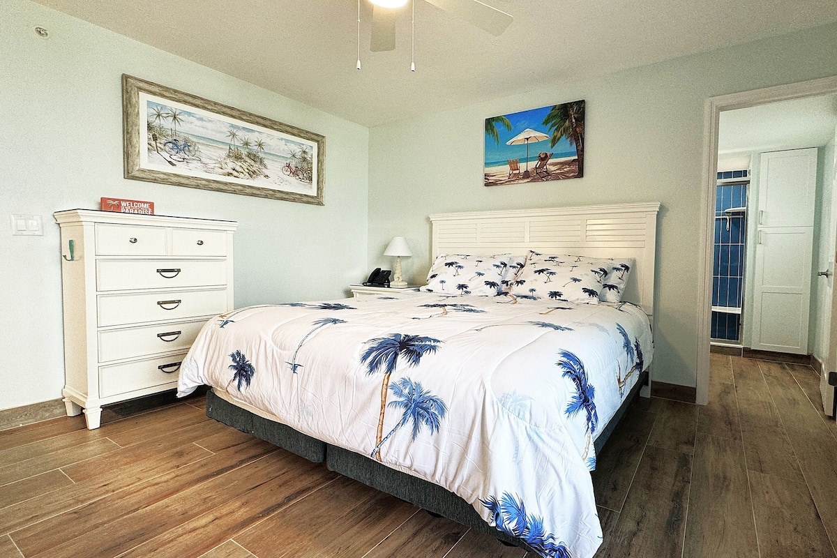 Une chambre à coucher comprenant un lit, une commode, une table de chevet et une porte donnant sur une autre pièce.