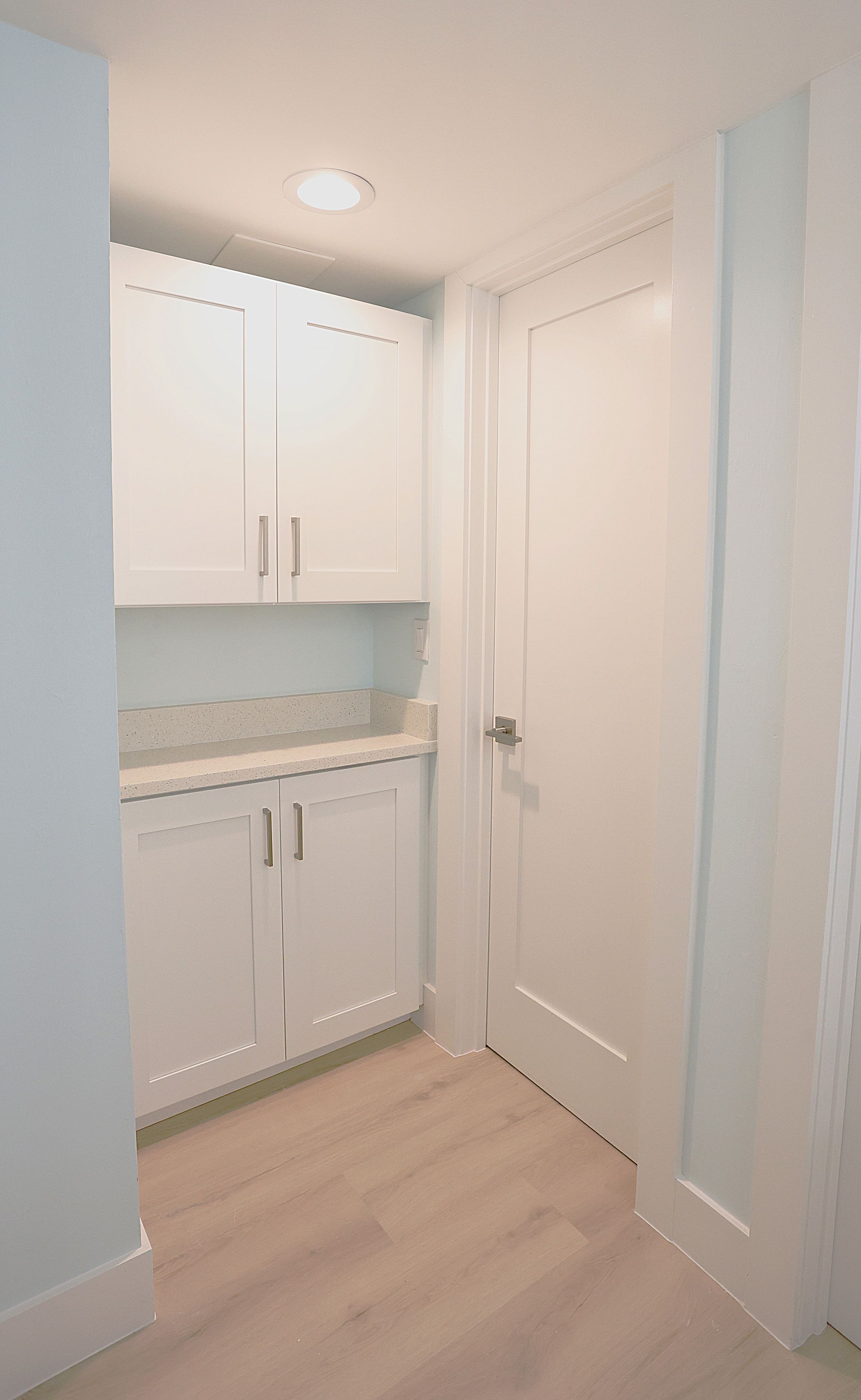 A small, clean kitchen with white cabinets, a countertop, and a door.