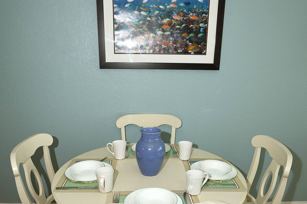 Une table à manger avec quatre chaises, un vase bleu, ainsi que des assiettes et des tasses blanches.