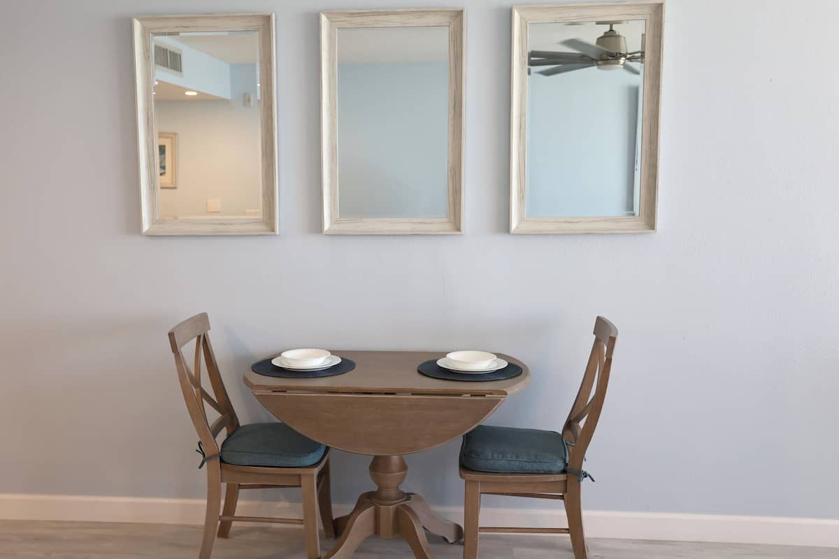 Un coin repas avec une table ronde, deux chaises et trois miroirs encadrés accrochés au mur.