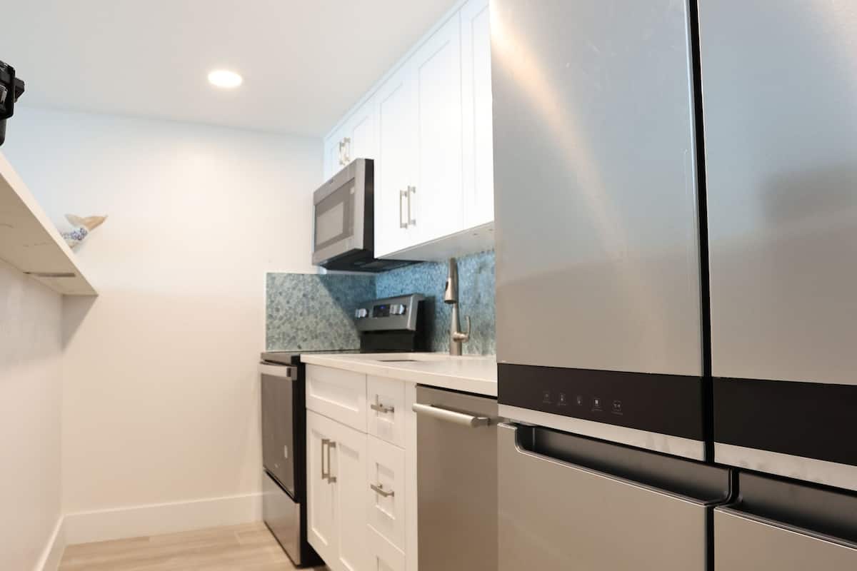 Une cuisine moderne dotée d’appareils électroménagers en acier inoxydable, de meubles blancs et d’un revêtement mural bleu.