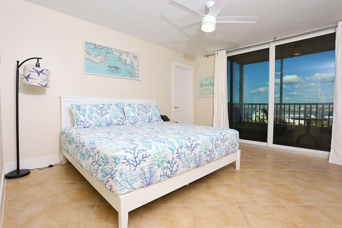 Une chambre à coucher avec un lit, un ventilateur de plafond, une carte accrochée au mur et un balcon donnant sur la mer.