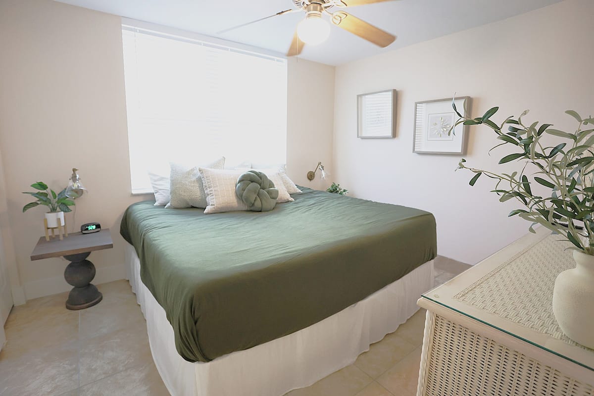 Une chambre à coucher avec un lit, une table de chevet avec une horloge, une fenêtre et un tableau accroché au mur.