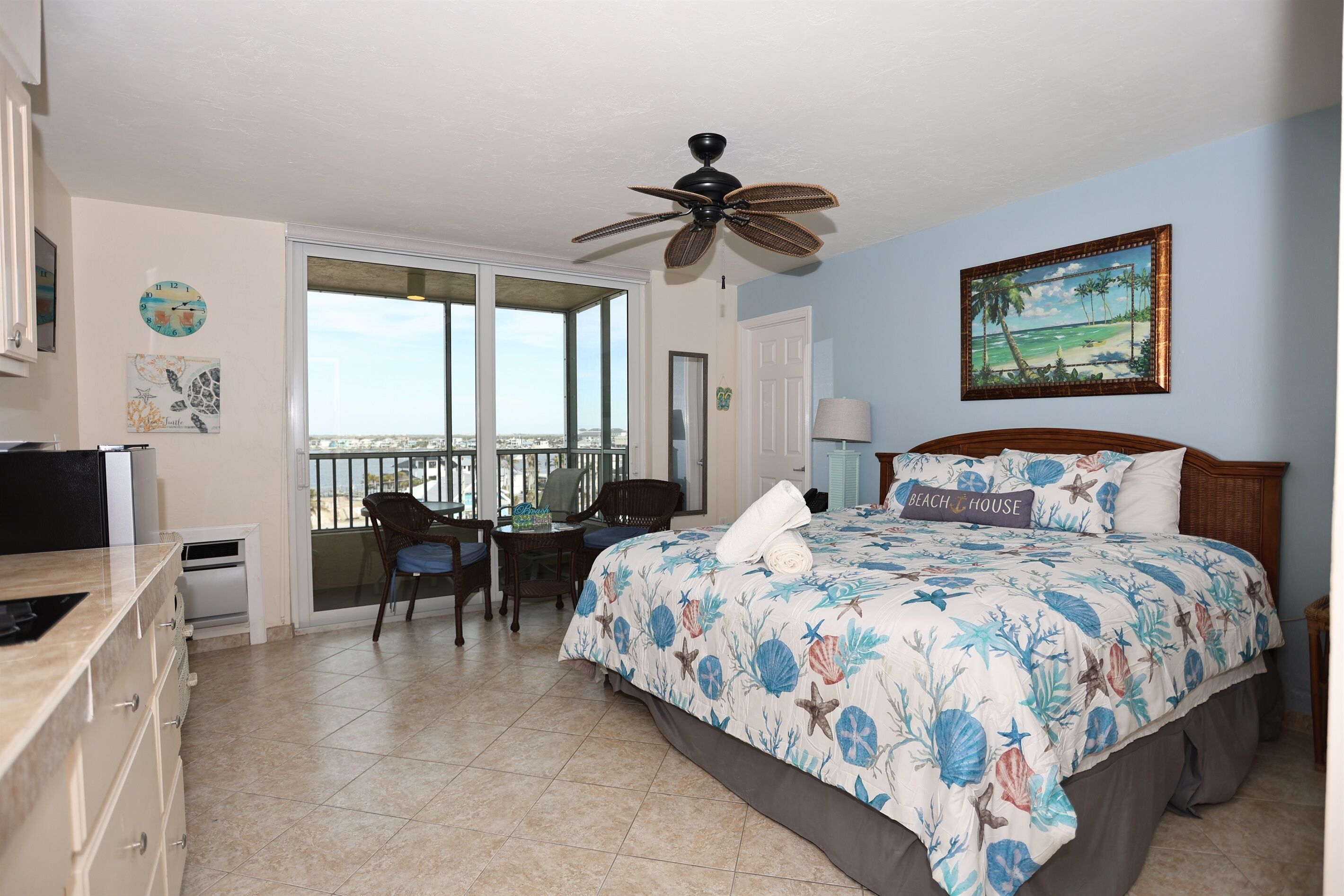 A bedroom with a bed, a ceiling fan, a window with a view, a desk, and a chair.